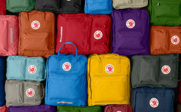 Colourful stack of Fjällräven Kånken Classic Backpacks in assorted shades, neatly arranged side by side.
