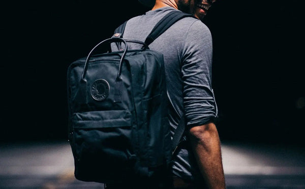 Man wearing a grey t-shirt carries the Kånken No.2 backpack in dark navy, showcasing the iconic Fjällräven circular logo.