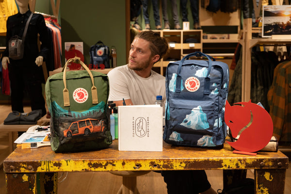Man at a workshop table with two special edition Fjällräven Kånken backpacks and outdoor gear, in Manchester Fjällräven store