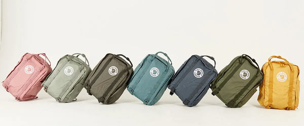 A range of Fjällräven Kånken backpacks in various colours displayed in a row on a white background, highlighting the variety of shades available.