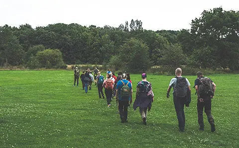Participants of the Fjällräven Walk in Manchester trek across a lush green field, with some sporting colourful Fjällräven backpacks.