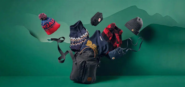 A collection of Fjällräven winter accessories, featuring colourful beanies, gloves, a patterned jumper, and a durable backpack, arranged against a green backdrop.
