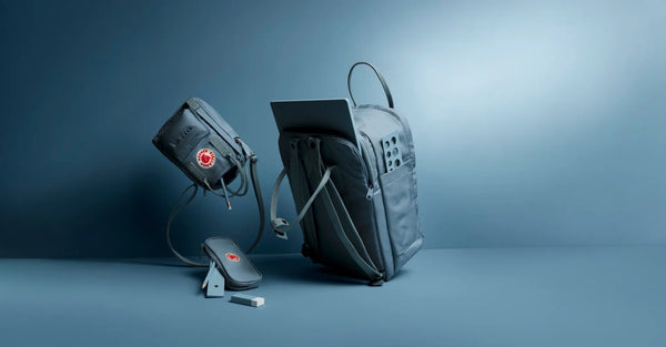 Two Fjällräven Kånken backpacks with electronic devices, showcasing a modern grey design with a USB charger against a blue backdrop.