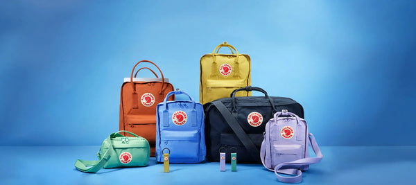 Fjällräven Kånken backpacks and bags in assorted colours and styles displayed against a bright blue background.