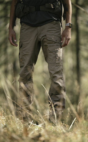 Man wearing Fjällräven men's trousers in a forest setting, showcasing durable and functional outdoor gear for adventurers.